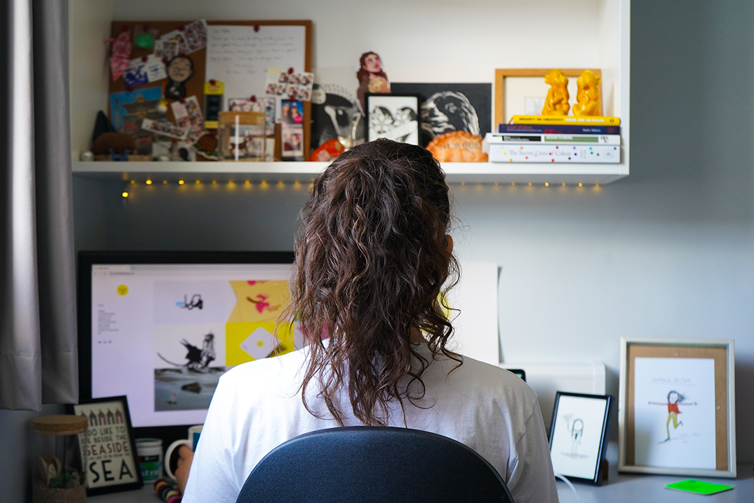 A student sits at a desk studying on a computer, facing away from the camera