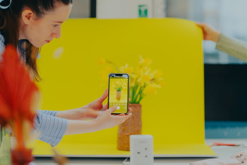 Yes Colours Visiting Lecture with Interiors student taking photo on phone of bright yellow background with flowers