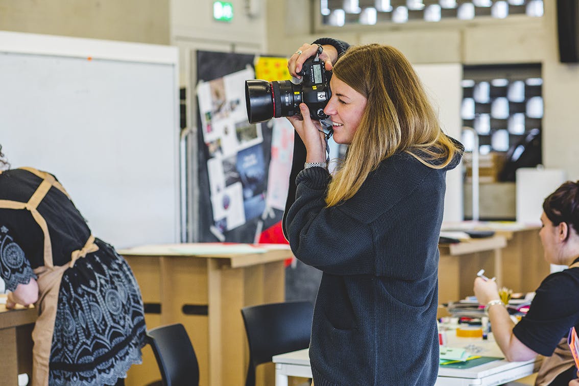 Clearing 2024 A smiling woman wearing a navy blue jumper holds a camera up to get a photo of an event