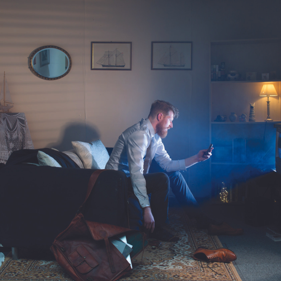 Set design by BA Hons Film Screen Arts students Man sits in dark room on sofa in front of TV