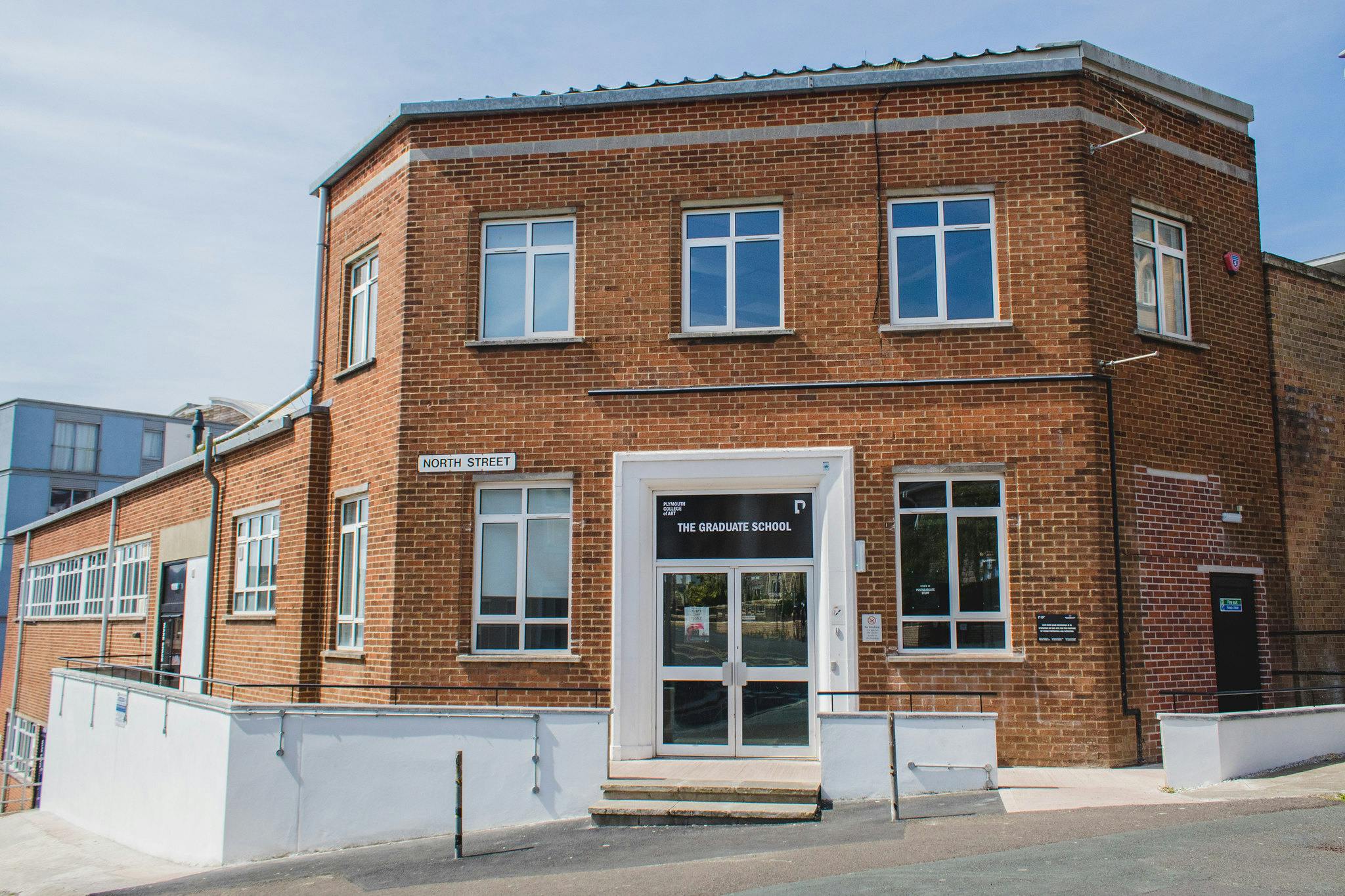 Our red brick Postgraduate Centre curves around the corner of the street with the blue sky and sun reflecting off the many windows.