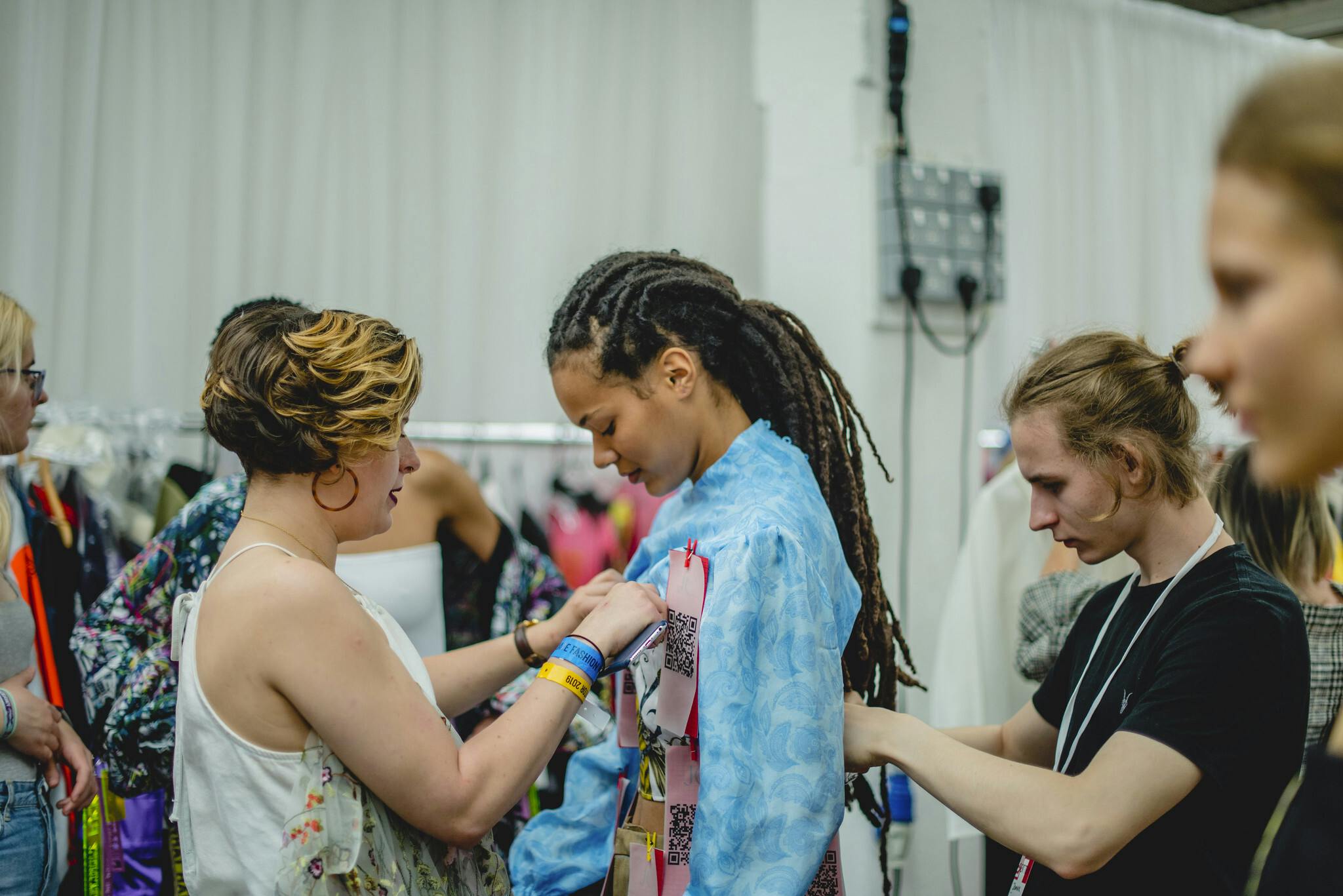 A student and model stand side-profile, styling a blue tie-die effect shirt in a busy dressing room.