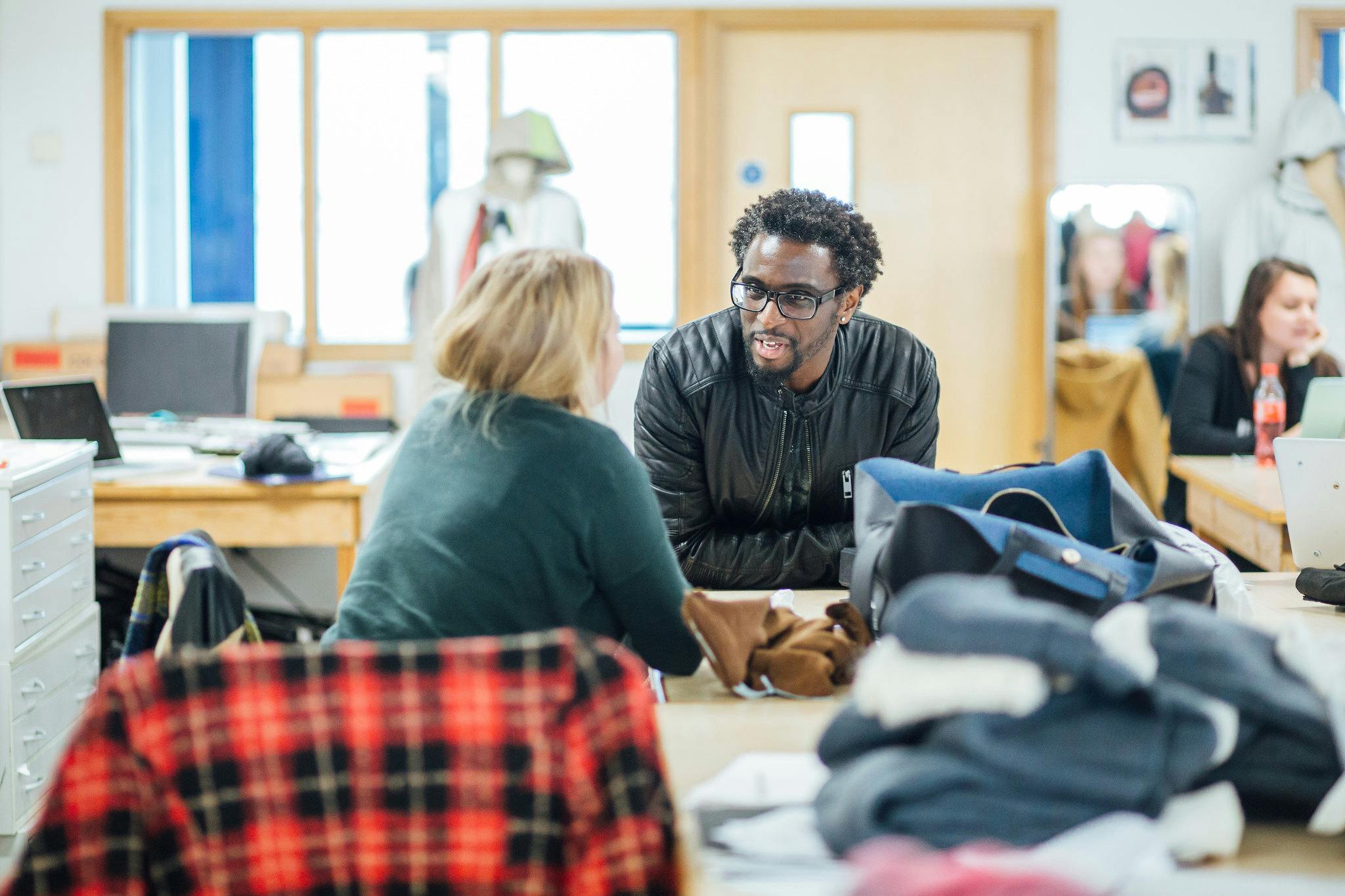 Consurgo founder Richie Manu leans on a desk and chats to a fashion student in our brightly lit fashion studio