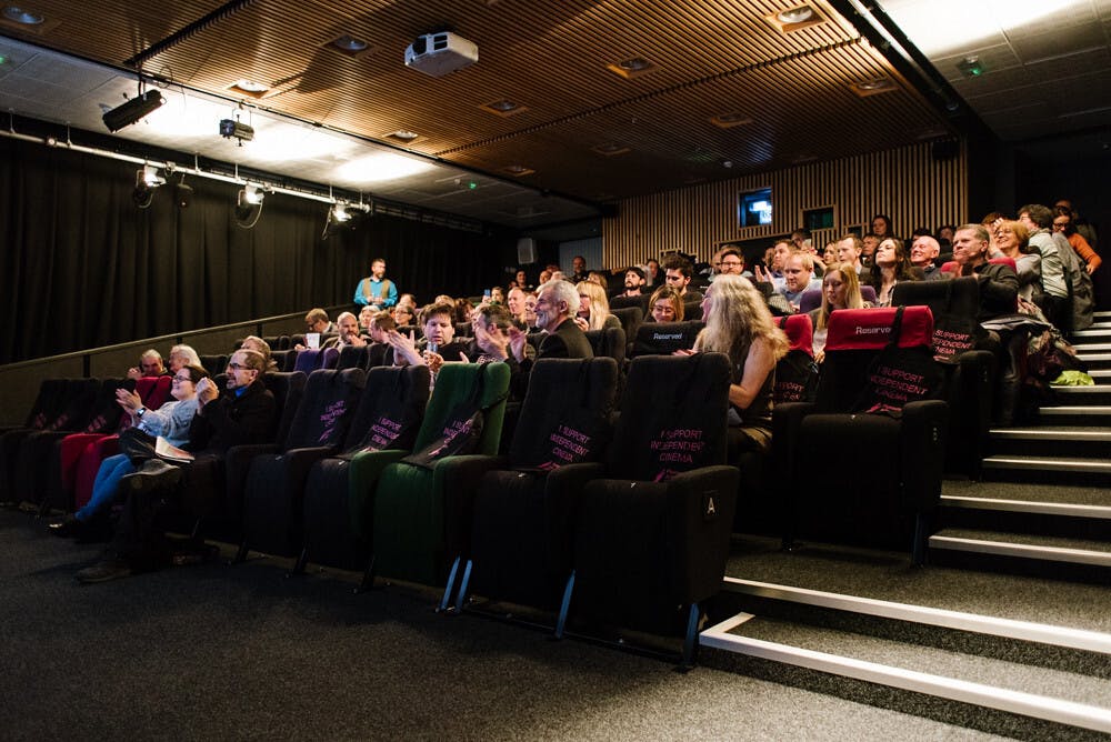 Grey, green, purple and pink cinema seats filled with people eagerly awaiting the film to start.