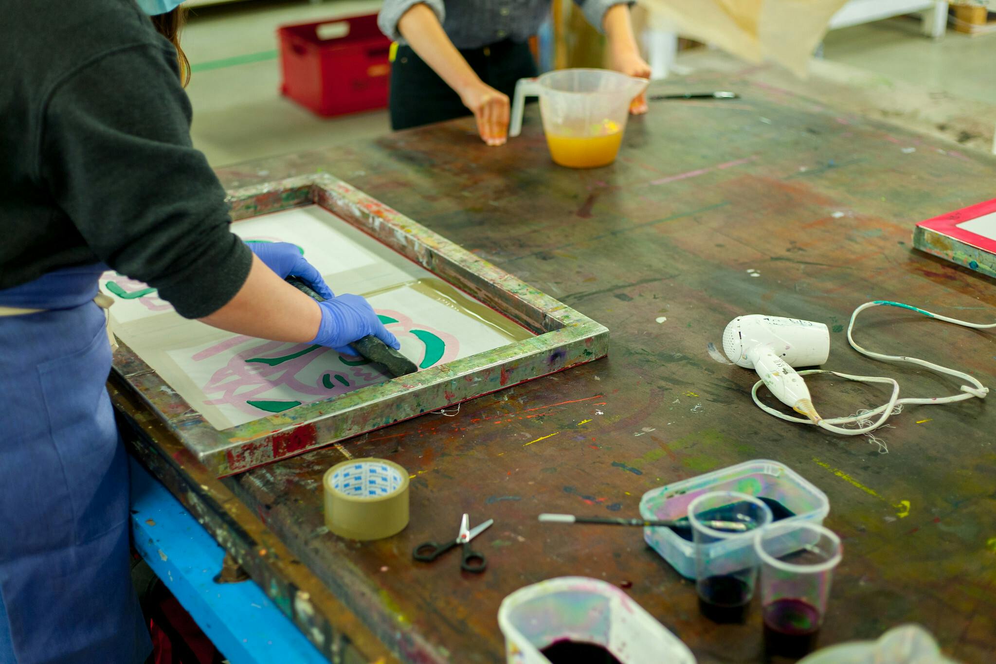 Hands pull ink across a textile screen laid flat on the table in order to transfer the design onto fabric