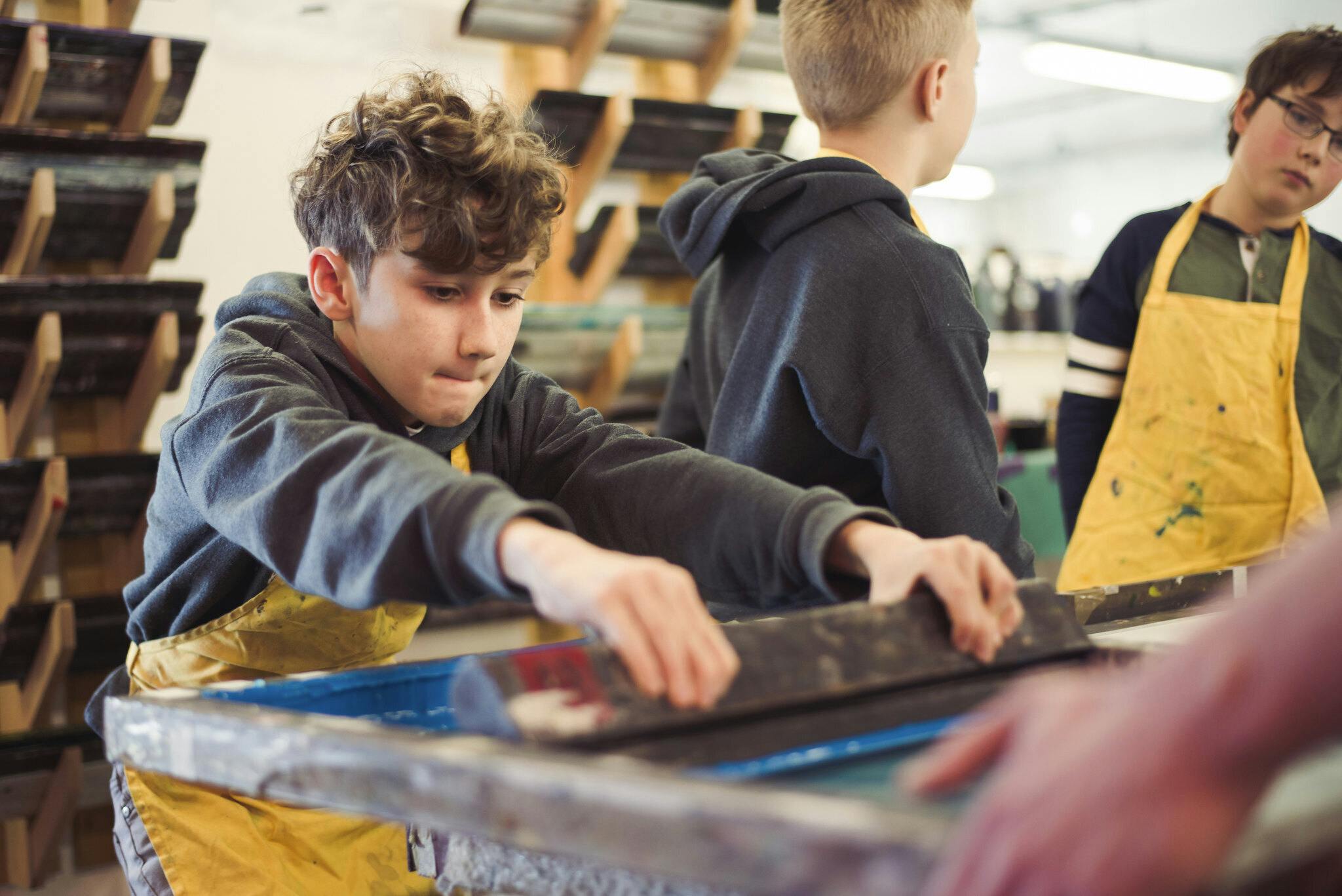 A young boy pulls a squeegee with all his might to pull ink from a screen in our print workshop.