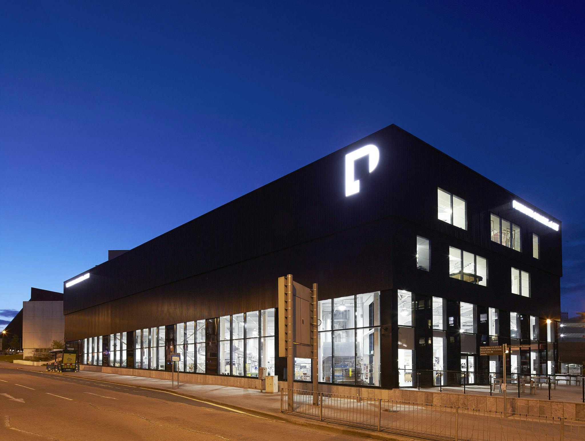 Charles Cross Building at night. Floor to ceiling windows are lit from the inside, allowing passers-by a peer into the Crafts Studios where glassblowing, pottery, jewellery-making and more take place.