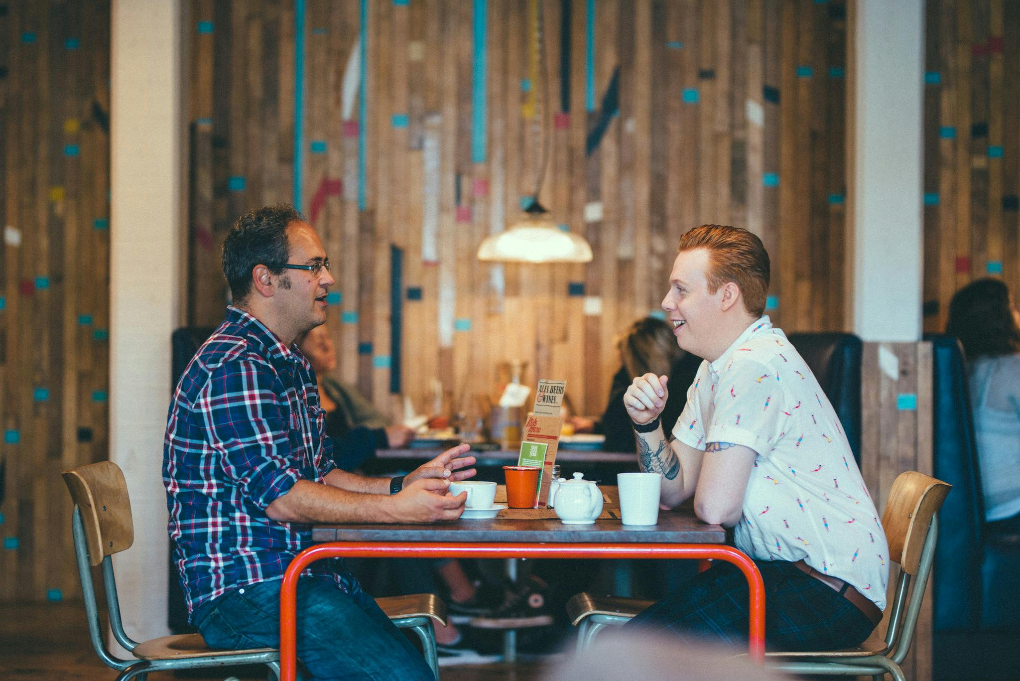 A lecturer and a student sit facing each other at a table in a cafe chatting amicably