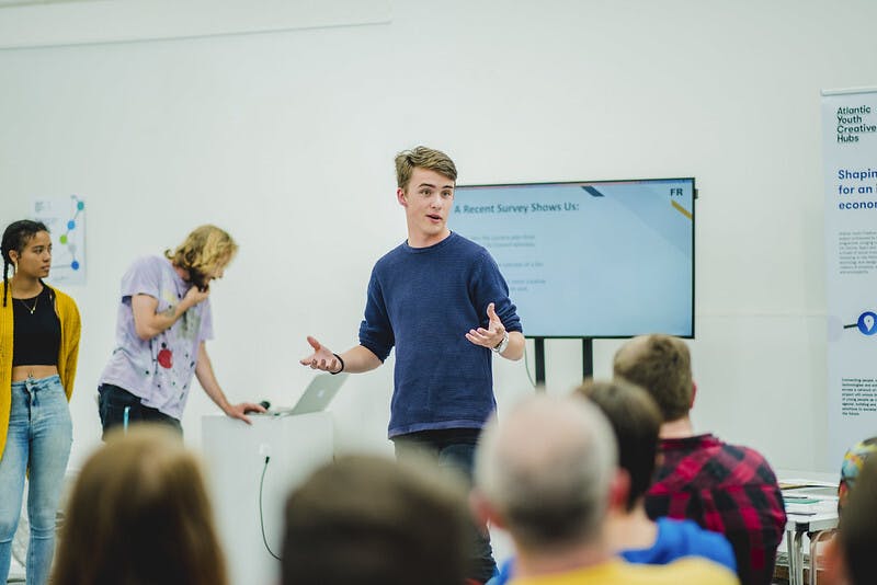 A male student in a blue jumper makes a presentation to a group of people AYCH Day 2 2018